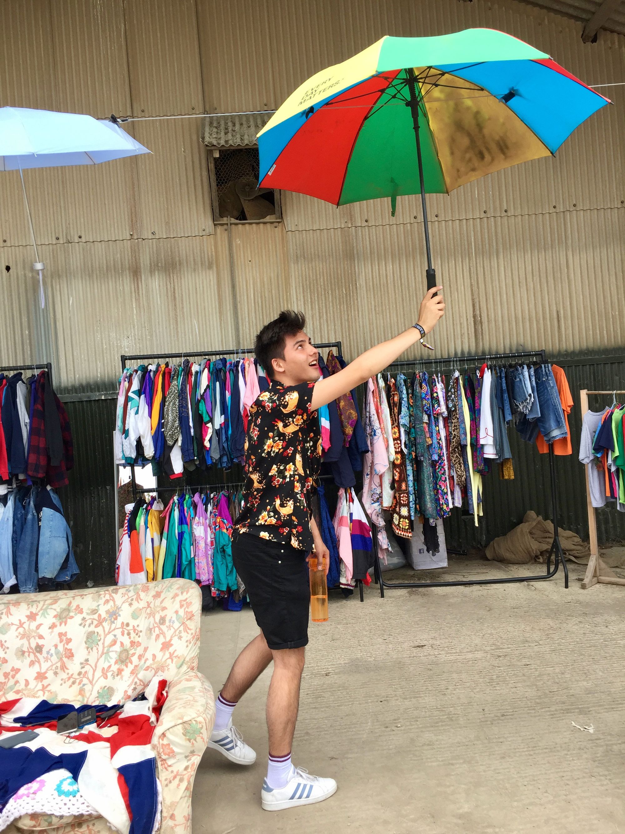 Chris at a festival, holding an umbrella and water bottle against a backdrop of vintage clothing